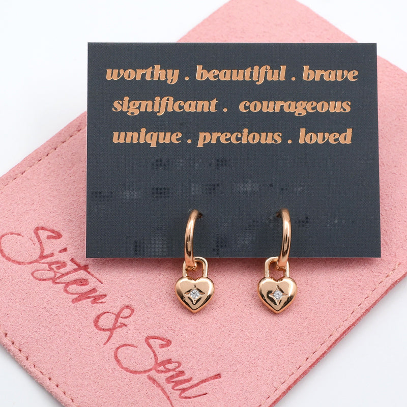 Rose gold heart-shaped earrings on a pink card with motivational text