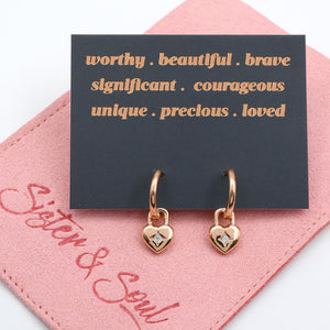Rose gold heart-shaped earrings on a pink card with motivational text