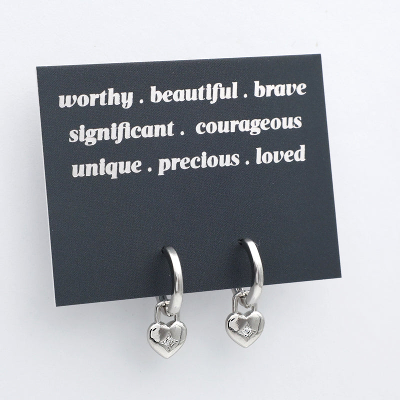 Silver heart-shaped earrings on a black card with positive affirmations on a white background