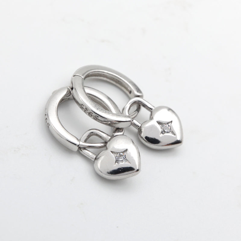 Silver key-shaped charm with heart and round pendants on a white background