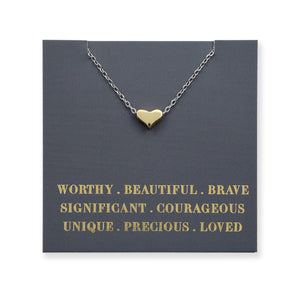Gold heart-shaped necklace on a dark gray card with motivational text