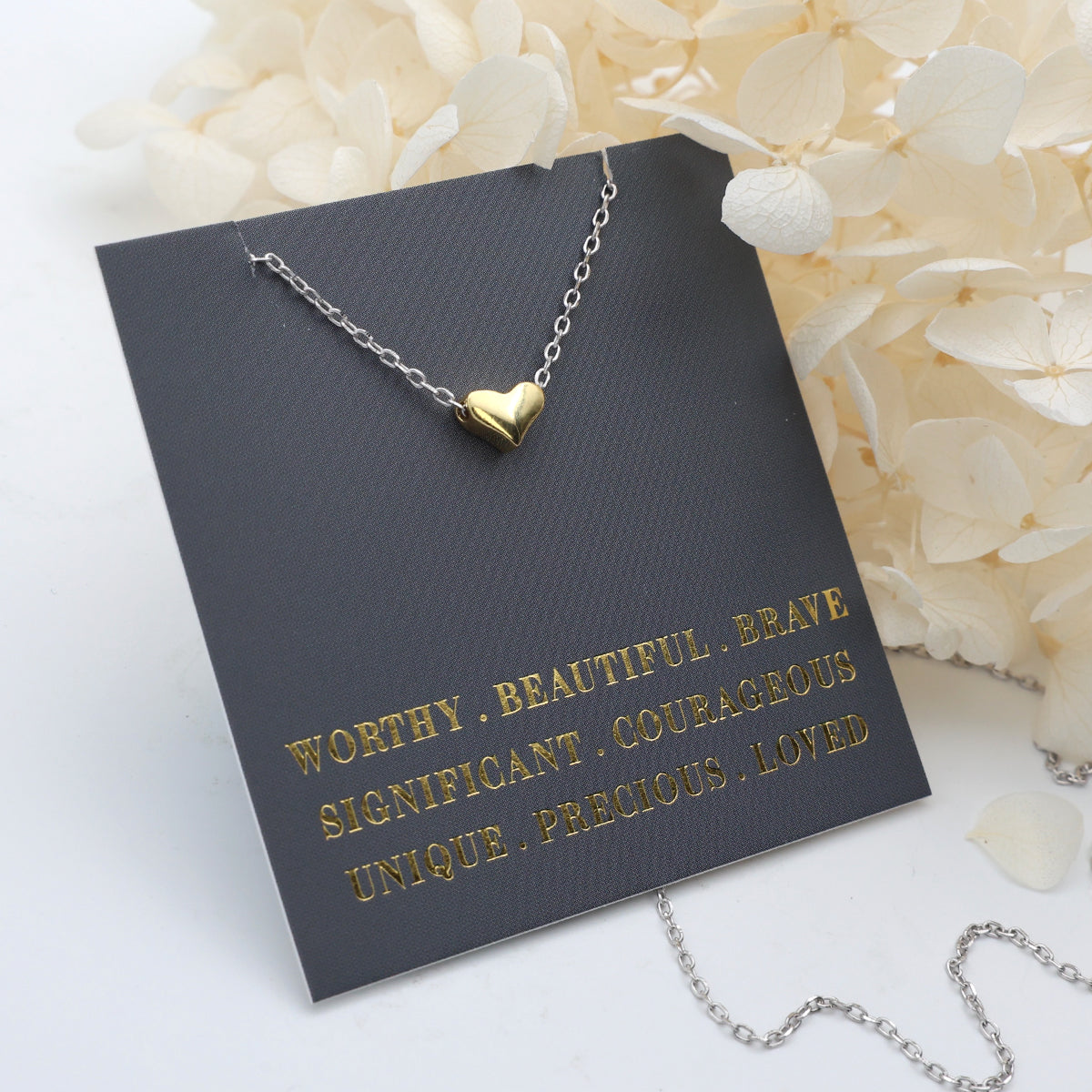 Gold heart-shaped necklace on a dark gray card with motivational text