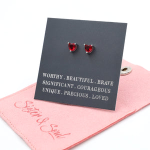 Red heart-shaped earrings on a card with motivational phrases, placed on a pink cloth with 'Sister & Soul' branding.