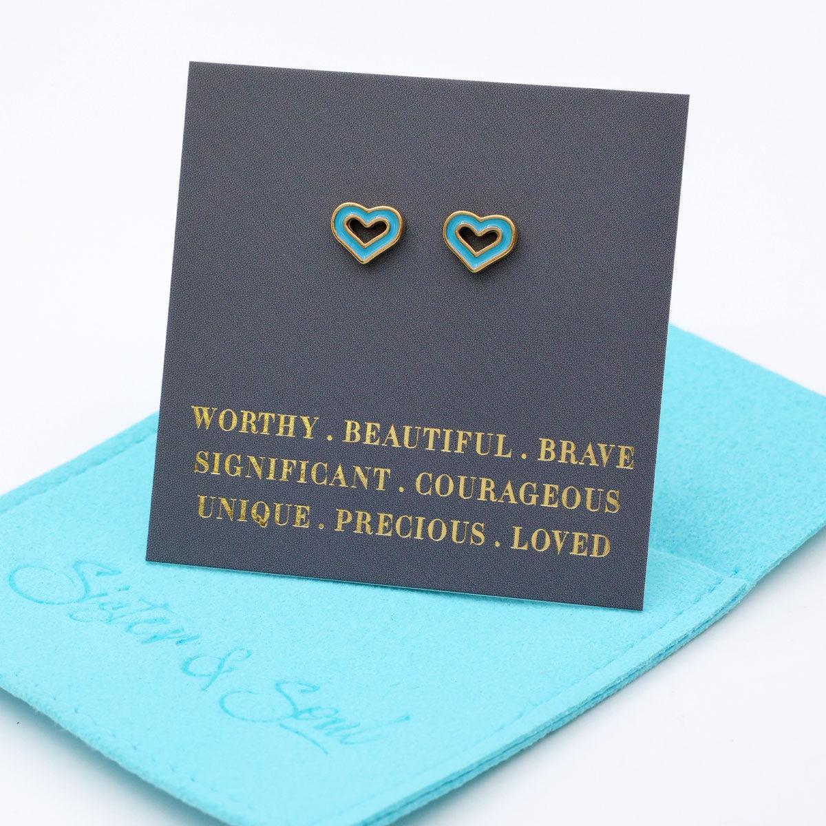 Heart-shaped earrings on a card with motivational phrases, placed on a blue cloth.