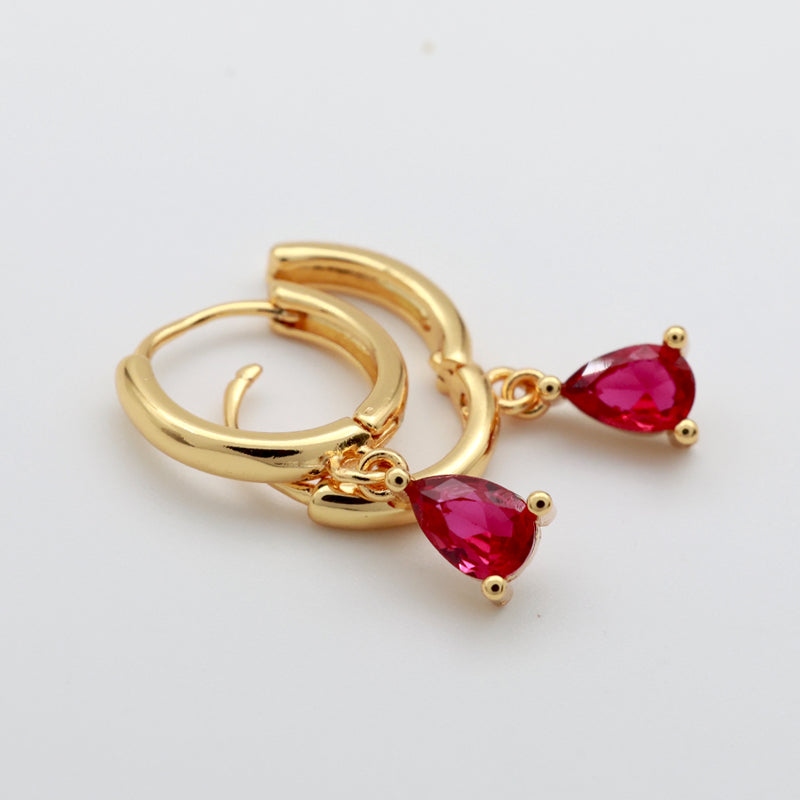Gold huggie hoop earrings with dangling teardrop-shaped red gemstones, shown on a plain light background.