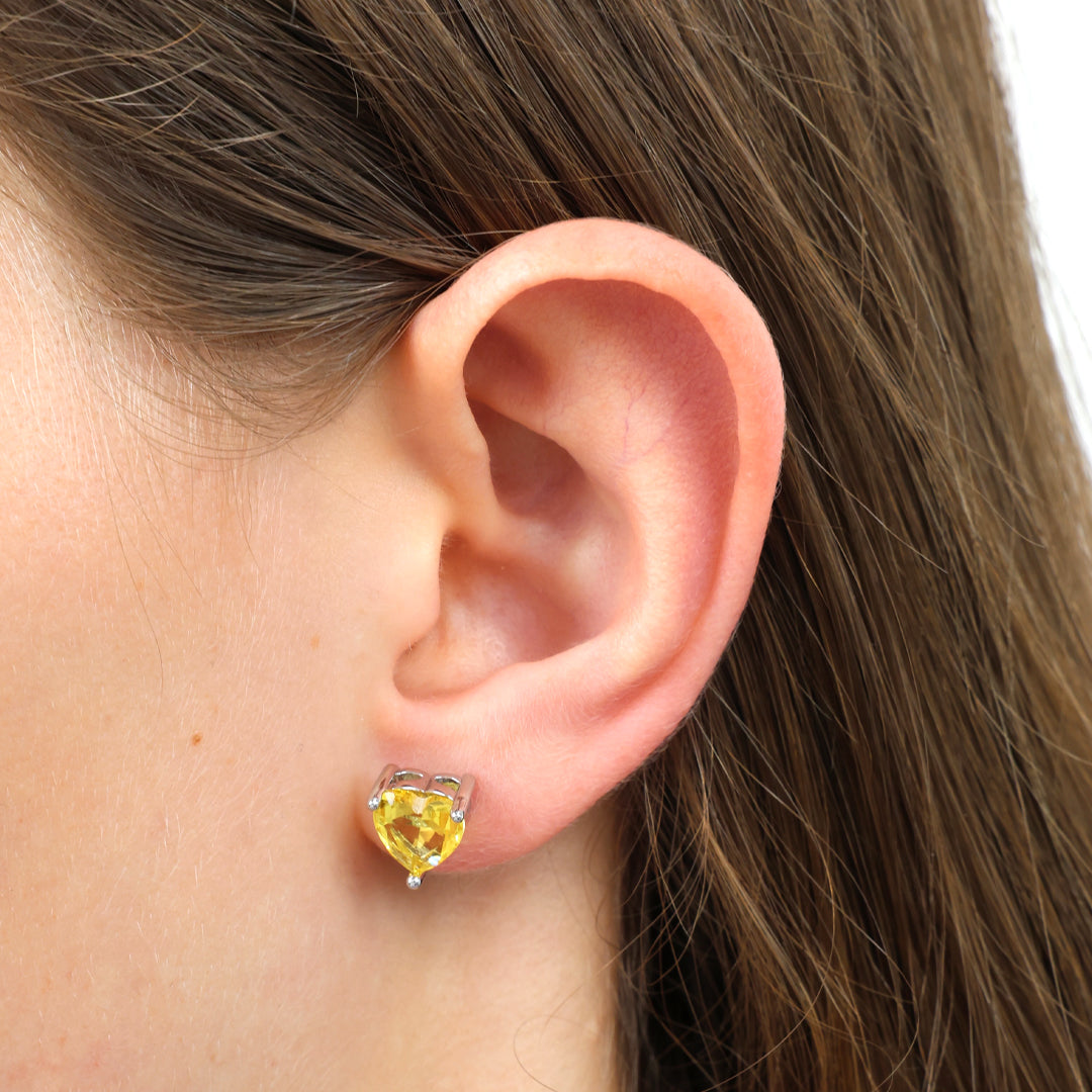 Close-up of an ear wearing a yellow heart-shaped earring with brown hair.