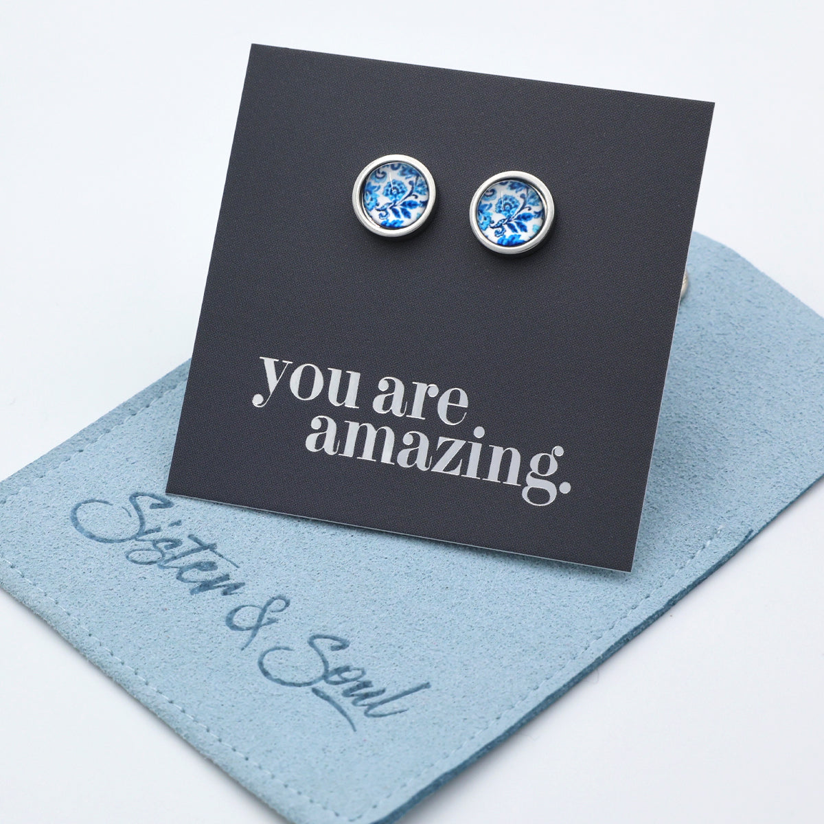 Pair of blue gemstone earrings on a card with 'you are amazing' text, placed on a light blue surface.