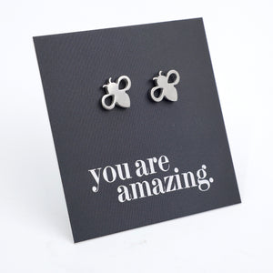 A pair of small silver bee stud earrings displayed on a dark gray square card that reads 'you are amazing.' in silver script, photographed on a clean white background.