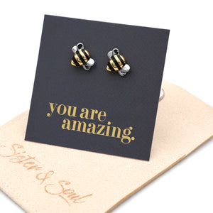 Bee-shaped earrings on a card with 'you are amazing' text, displayed on a beige surface.