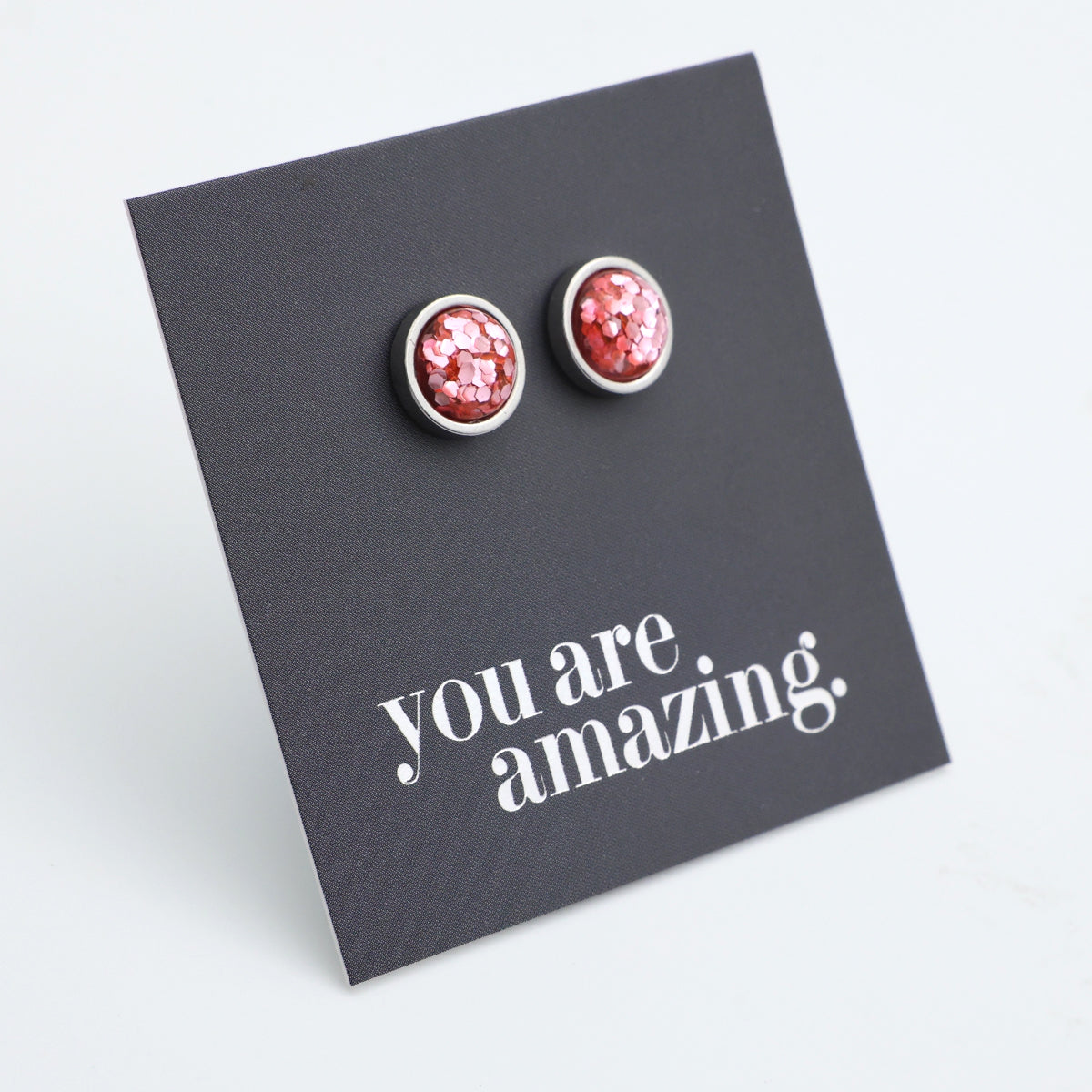 Red glittery stud earrings on a black card with 'you are amazing' text