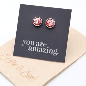 Pink glittery stud earrings on a card with 'you are amazing' text, displayed on a beige card with 'Sister & Swag' branding.