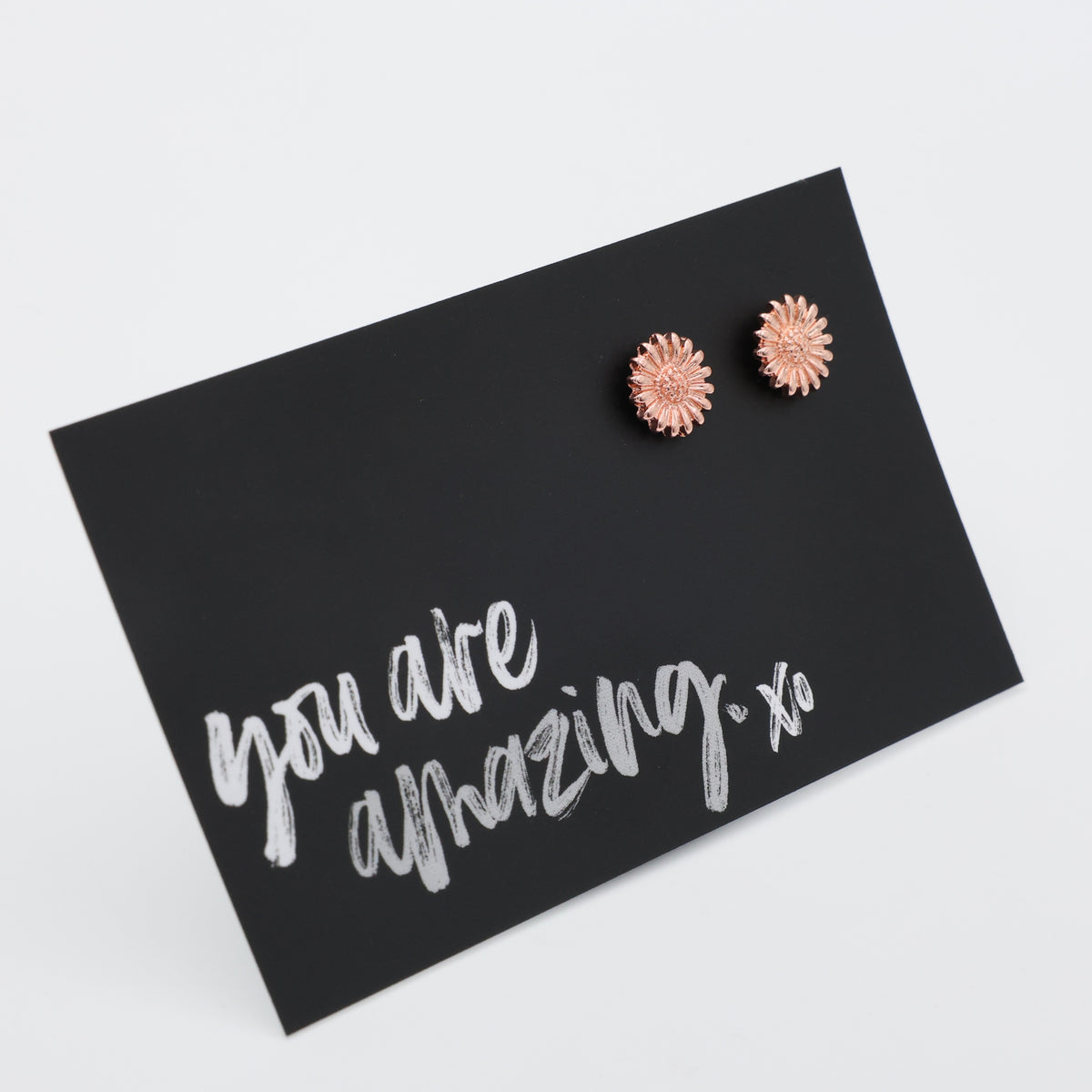 Rose gold flower earrings on a black card with 'you are amazing' text