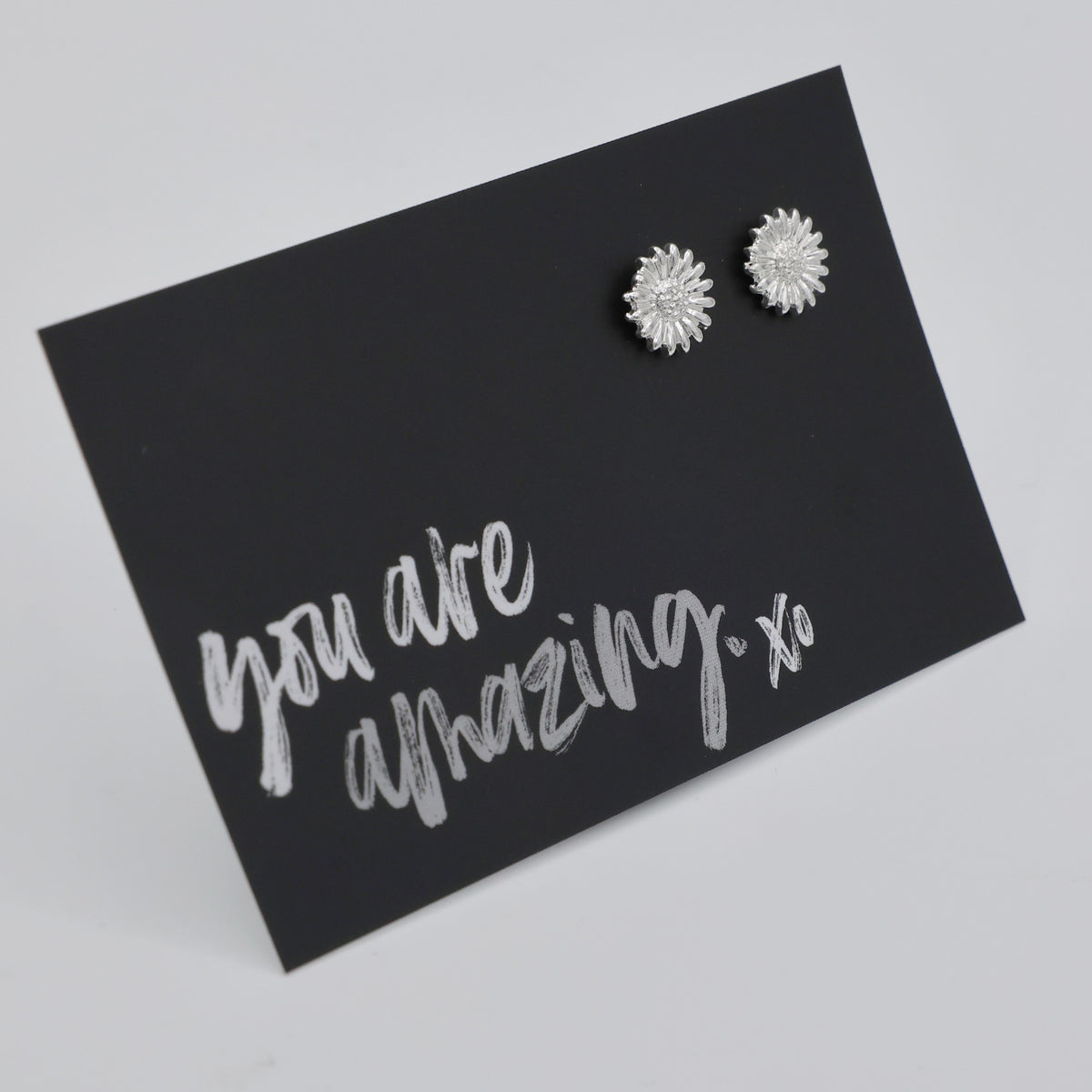 Silver floral earrings on a black card with 'you are amazing xo' text.