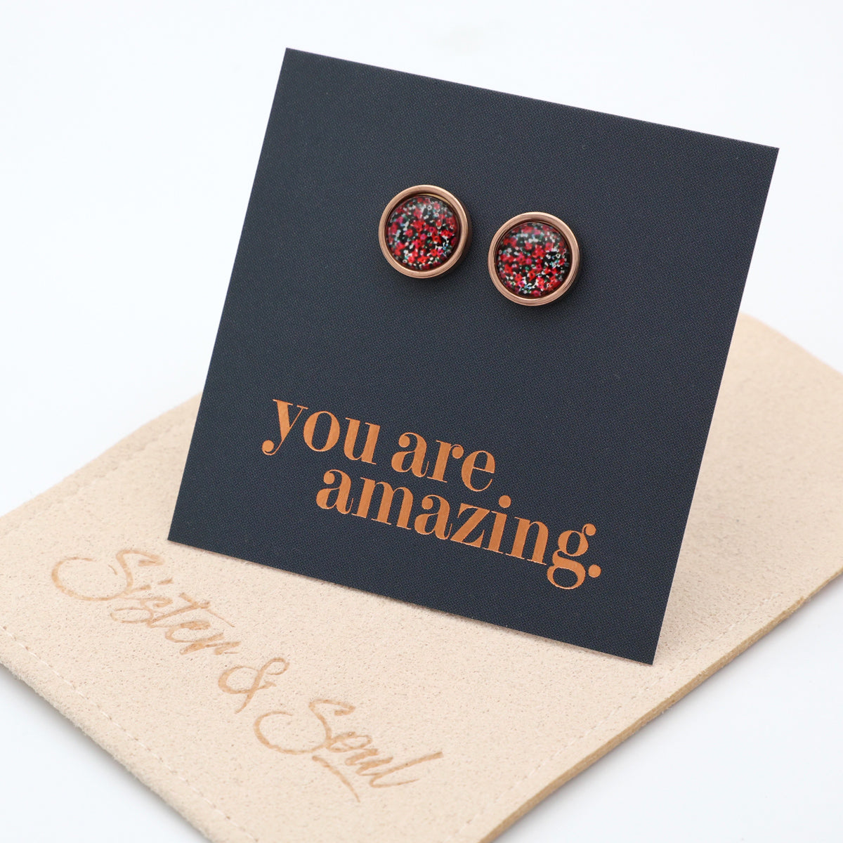 Pair of earrings on a card with 'you are amazing' text, placed on a beige surface.