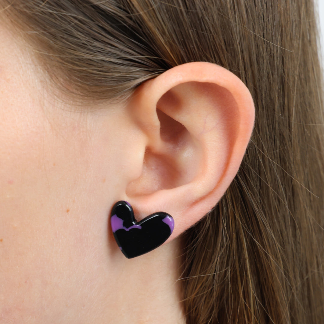 A pair of heart-shaped stud earrings with a glossy black and purple marbled pattern, mounted on a white display card that reads 'YOU ARE BEAUTIFUL' in black text.
