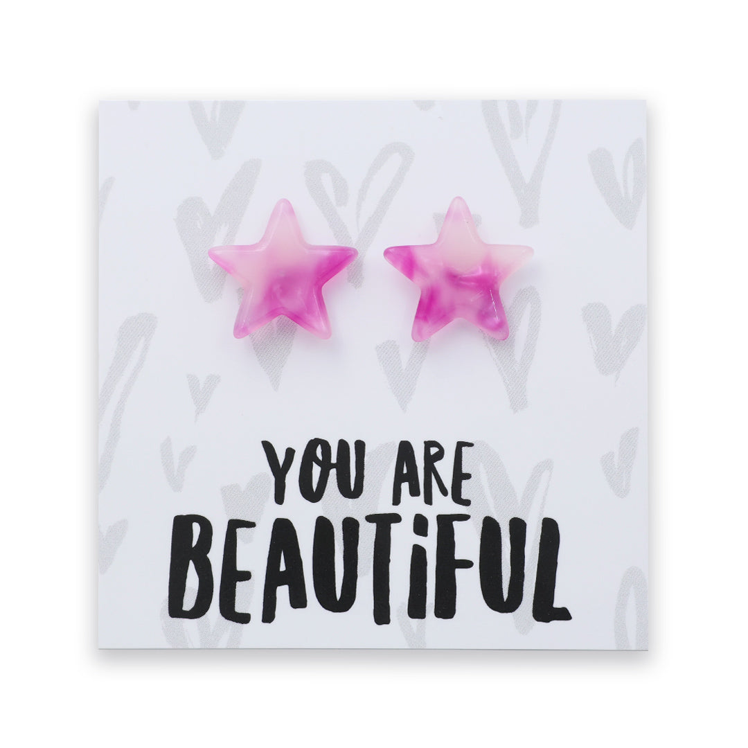 A pair of pink star-shaped stud earrings displayed on a white square card with the text 'YOU ARE BEAUTIFUL' in black lettering.