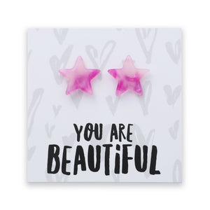 A pair of pink star-shaped stud earrings displayed on a white square card with the text 'YOU ARE BEAUTIFUL' in black lettering.