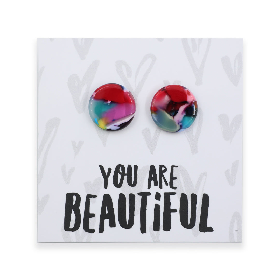 A pair of round acrylic stud earrings with a colorful marbled pattern in red, pink, blue, and yellow, displayed on a white backing card that reads 'YOU ARE BEAUTIFUL' in black text.