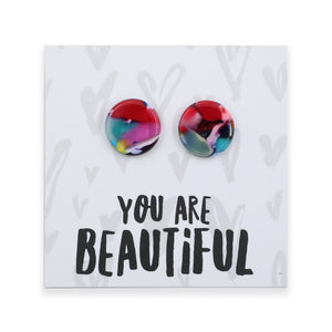 A pair of round acrylic stud earrings with a colorful marbled pattern in red, pink, blue, and yellow, displayed on a white backing card that reads 'YOU ARE BEAUTIFUL' in black text.
