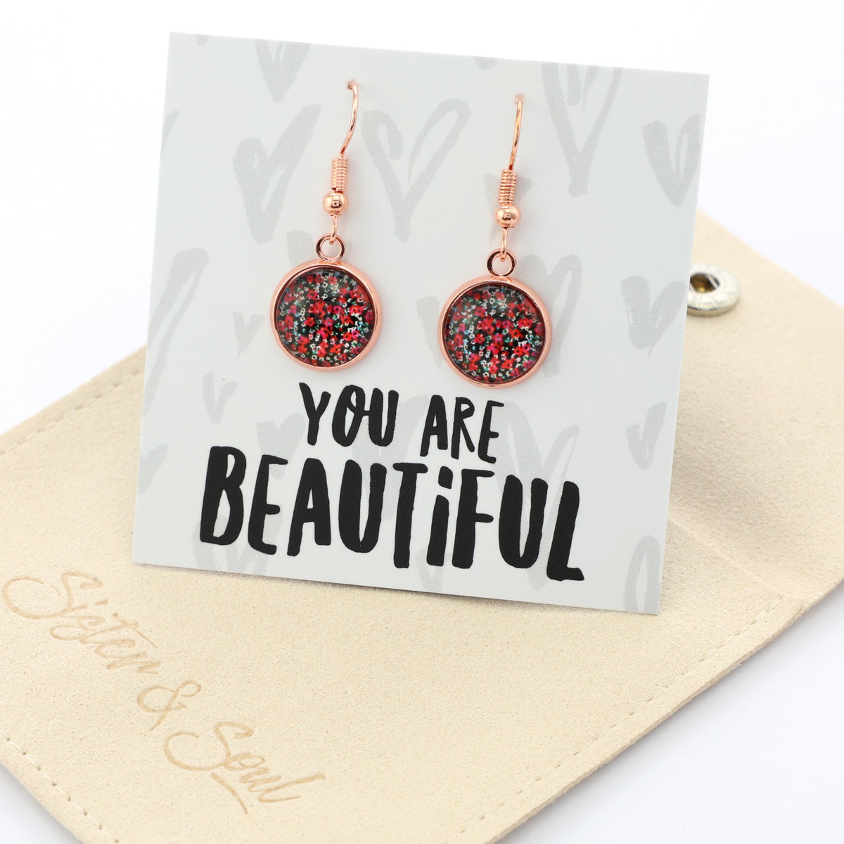 Rose gold earrings on a card with 'You are Beautiful' text, placed on a beige surface.