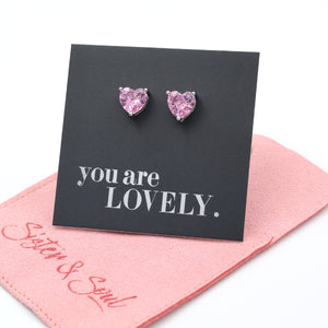 Heart-shaped pink earrings on a 'you are LOVELY' card with a pink pouch underneath.