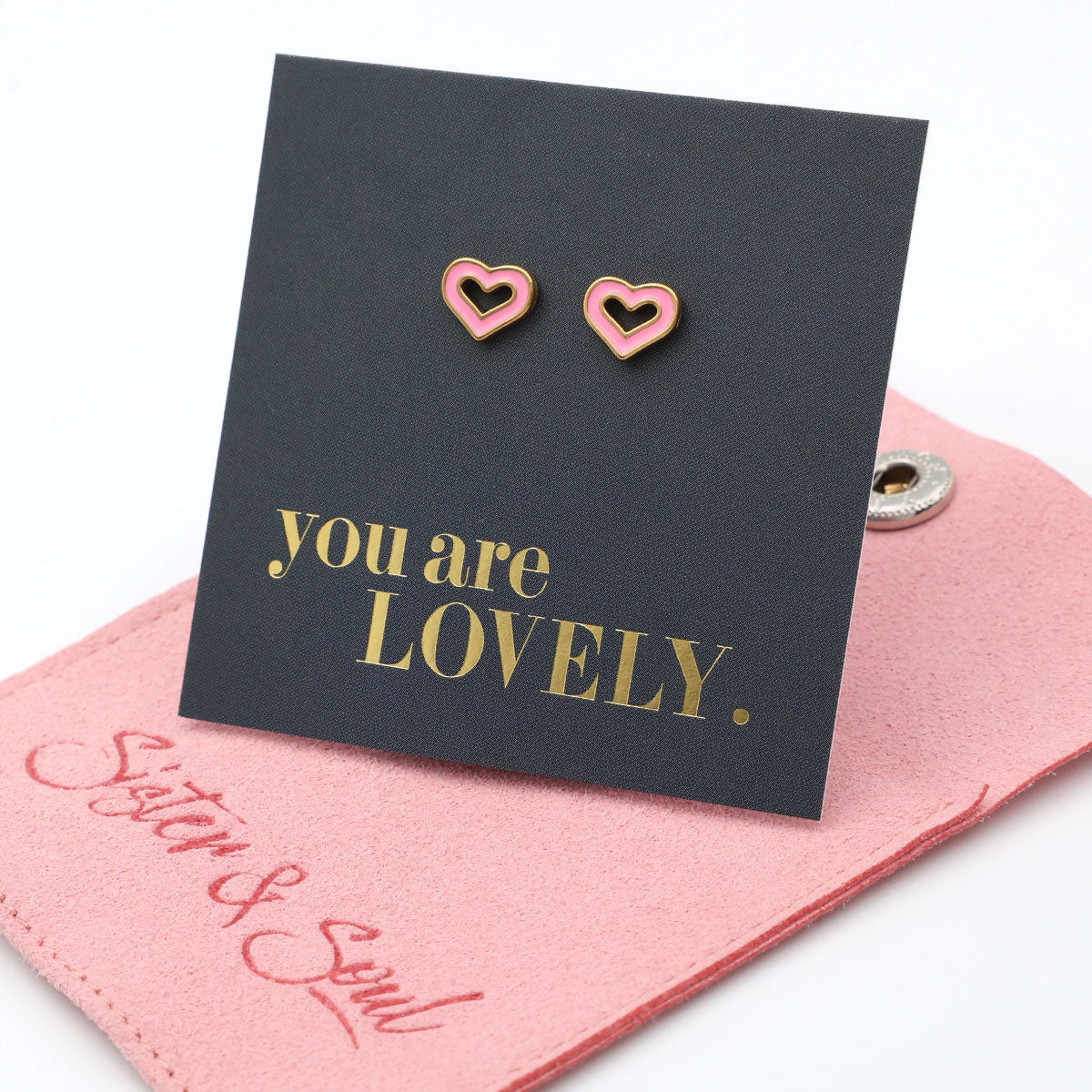 Heart-shaped earrings on a card with 'you are LOVELY' text, placed on a pink surface with 'Sister & Soul' branding.