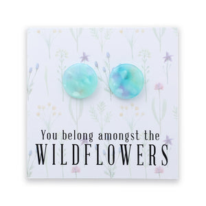 A pair of round, iridescent light blue and green stud earrings displayed on a white floral backing card with the text 'You belong amongst the WILDFLOWERS'.
