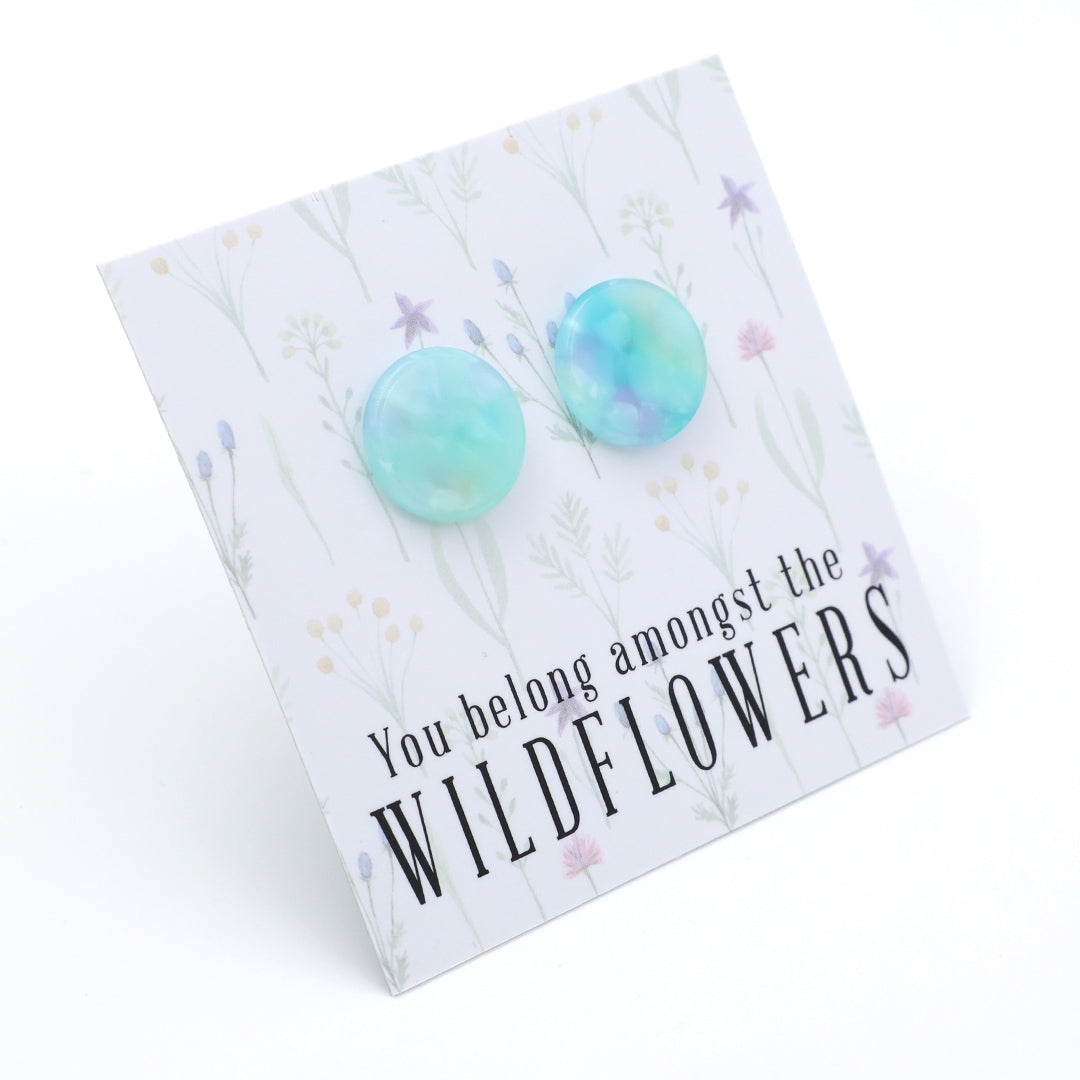 A pair of round, marbled turquoise and light blue stud earrings displayed on a white floral backing card that reads 'You belong amongst the WILDFLOWERS'.
