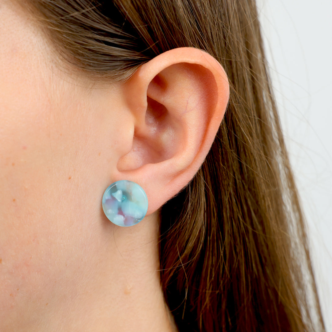 A pair of round, iridescent light blue and green stud earrings displayed on a white floral backing card with the text 'You belong amongst the WILDFLOWERS'.