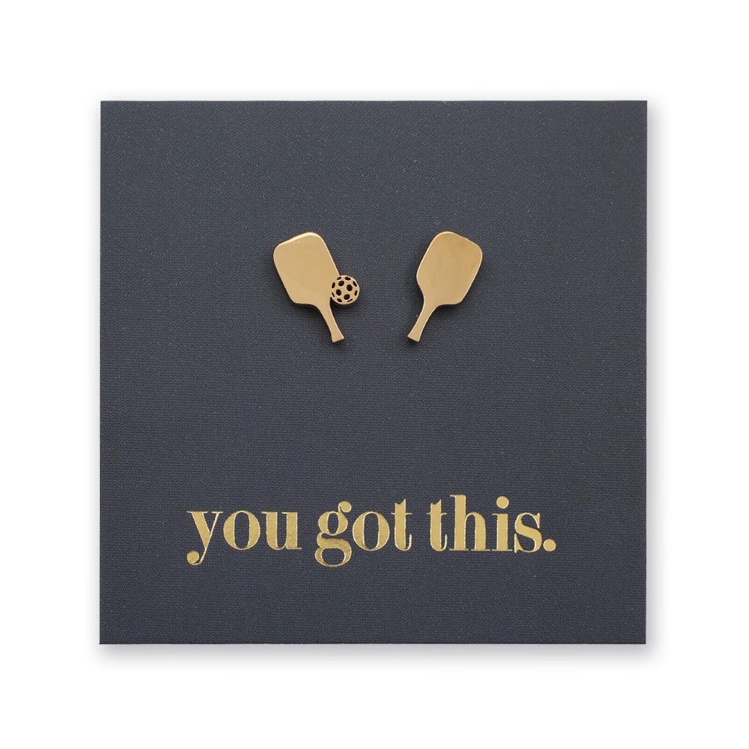 Four square cards arranged on a white background, each with a small pair of pickle ball paddle-shaped studs and the phrase 'you got this.' in different colors: black, rose gold, gold, and silver.