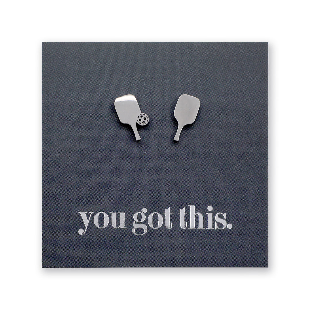A pair of silver-toned pickle ball paddle-shaped stud earrings displayed on a dark charcoal square backing card that reads 'you got this.' in silver lowercase text.