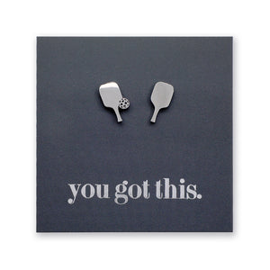 A pair of silver-toned pickle ball paddle-shaped stud earrings displayed on a dark charcoal square backing card that reads 'you got this.' in silver lowercase text.