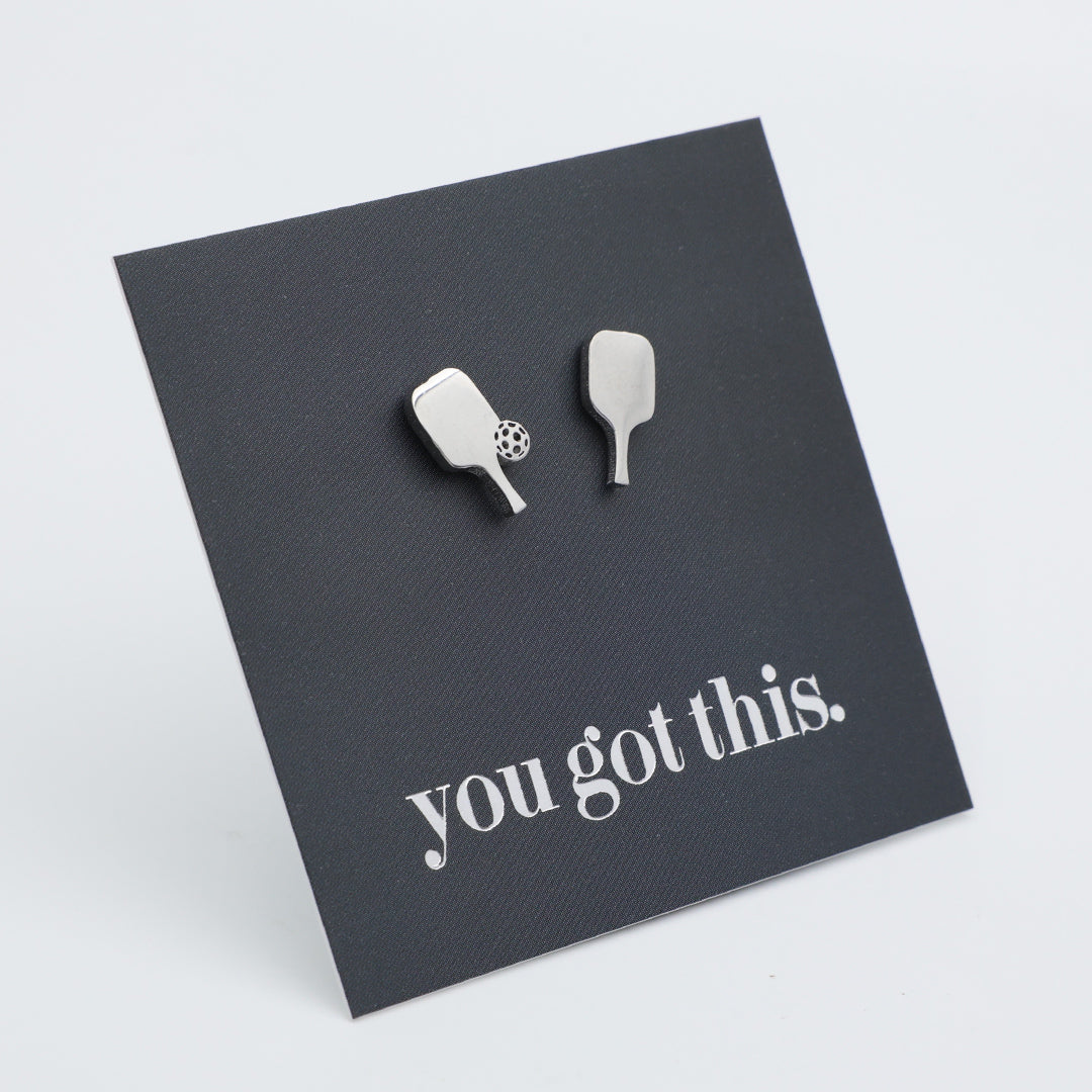 A pair of silver pickle ball paddle-shaped-shaped stud earrings displayed on a dark gray square card that reads 'you got this.' in white script, photographed on a light gray background.