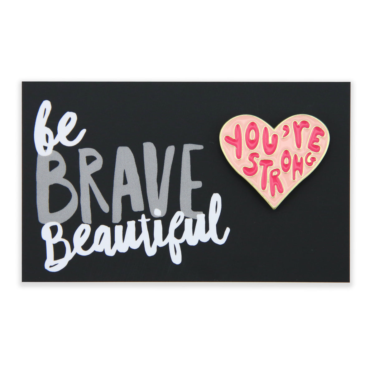 An enamel badge pin with a black background featuring white text 'be BRAVE Beautiful' and a pink heart with the phrase 'YOU'RE STRONG'.