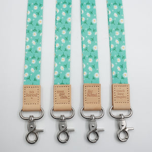 Aqua Daisies lanyards with white daisy print, tan tabs showing all four messages and silver-tone clasps.