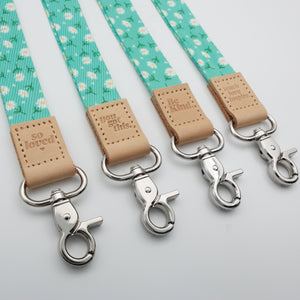 Angled close-up of Aqua Daisies lanyards with tan So Loved, You Got This, Be Kind and Teach Love Inspire tabs and silver-tone clasps.