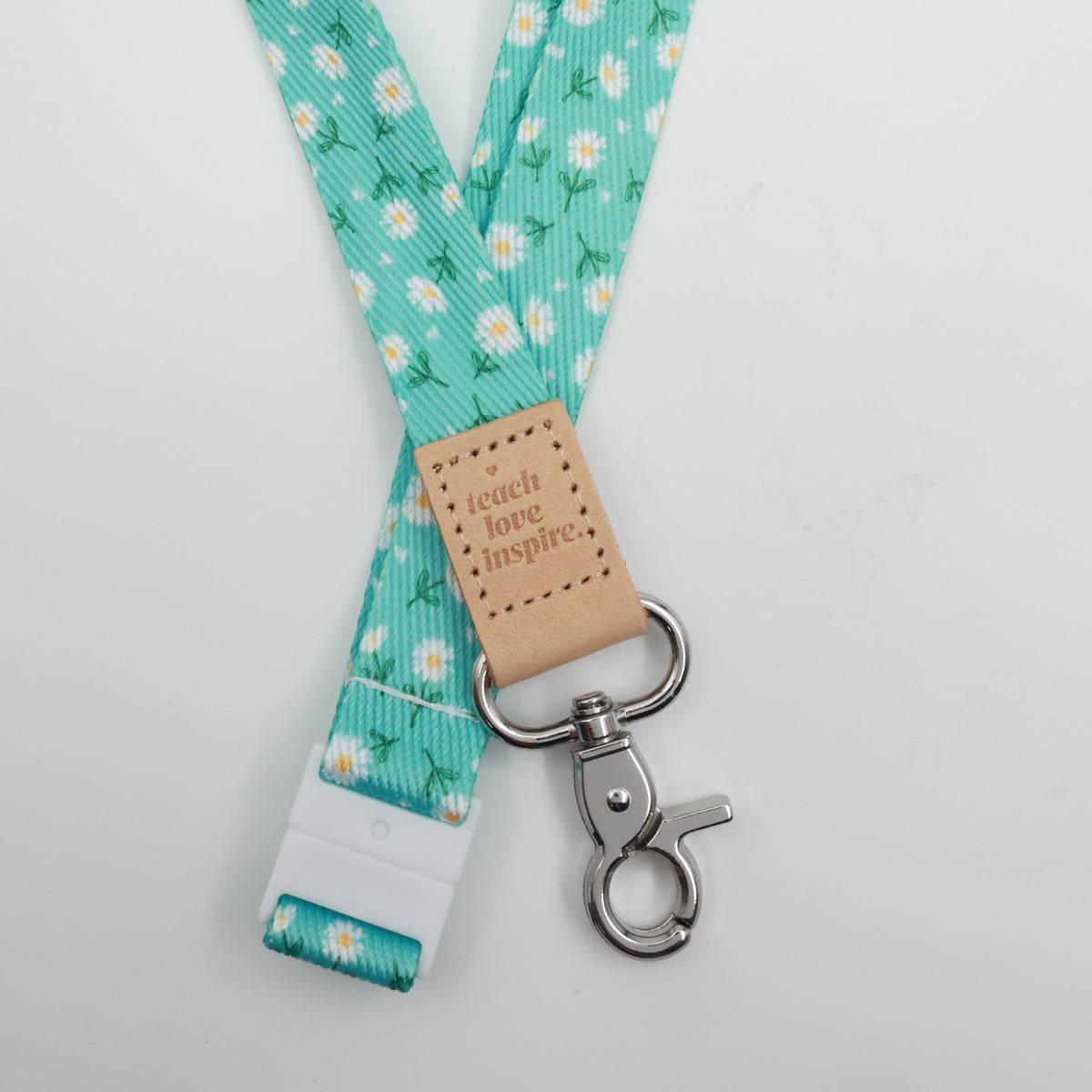 Aqua Daisies lanyard with white flowers, a tan Teach Love Inspire tab, silver-tone clasp and white breakaway fastening.