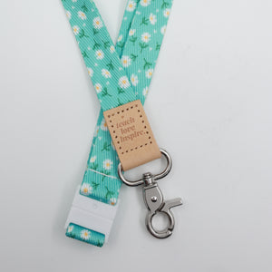 Aqua Daisies lanyard with white flowers, a tan Teach Love Inspire tab, silver-tone clasp and white breakaway fastening.