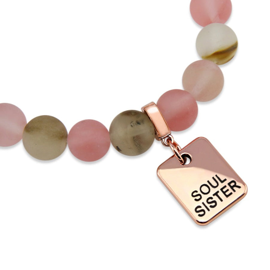 A collection of stone bracelets with rose gold charms, featuring beads in pink and earthy tones, with charms that say 'LOVE', 'I AM ENOUGH', 'CHOOSE KIND', and 'LOVE MY TRIBE'.