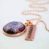 Red, blue, and orange patterned print pendant necklace with rose gold ball chain and Strength word charm.