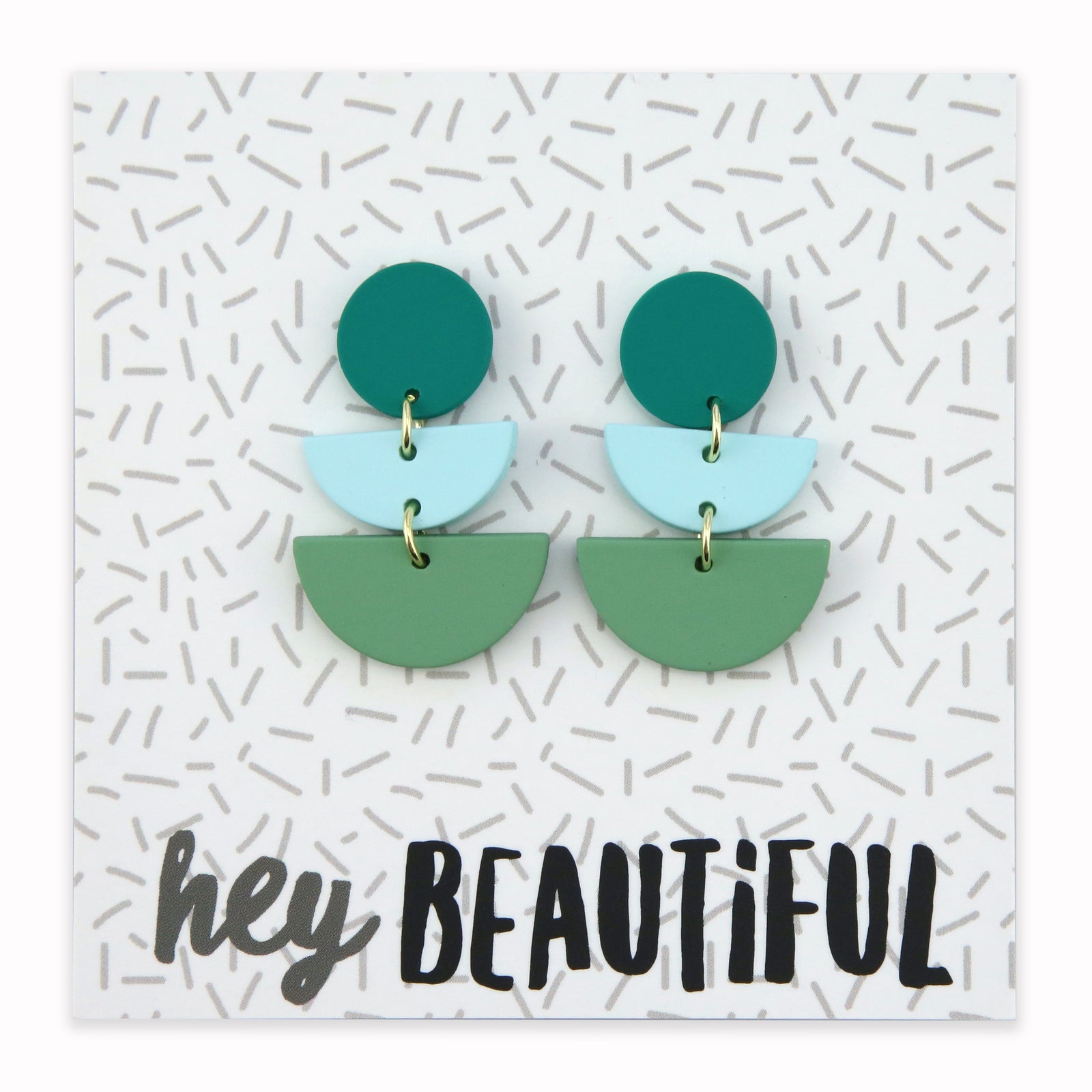 Acrylic and polymer clay statement dangle earrings in shasdes of green on a card that says 'hey beautiful'.