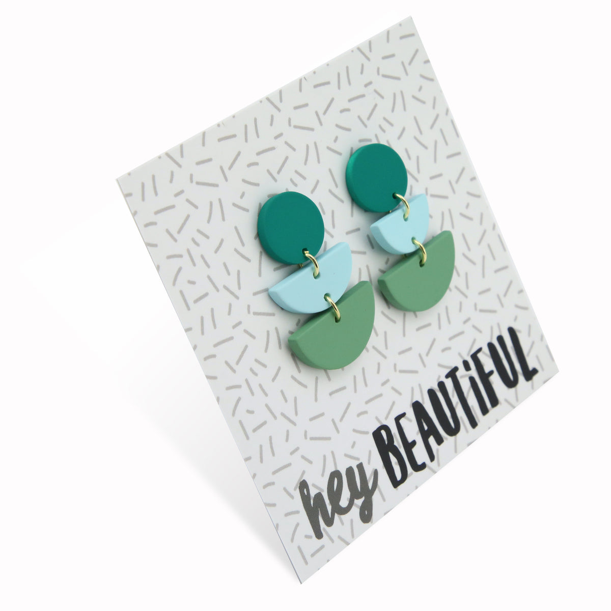 Acrylic and polymer clay statement dangle earrings in shasdes of green on a card that says 'hey beautiful'.