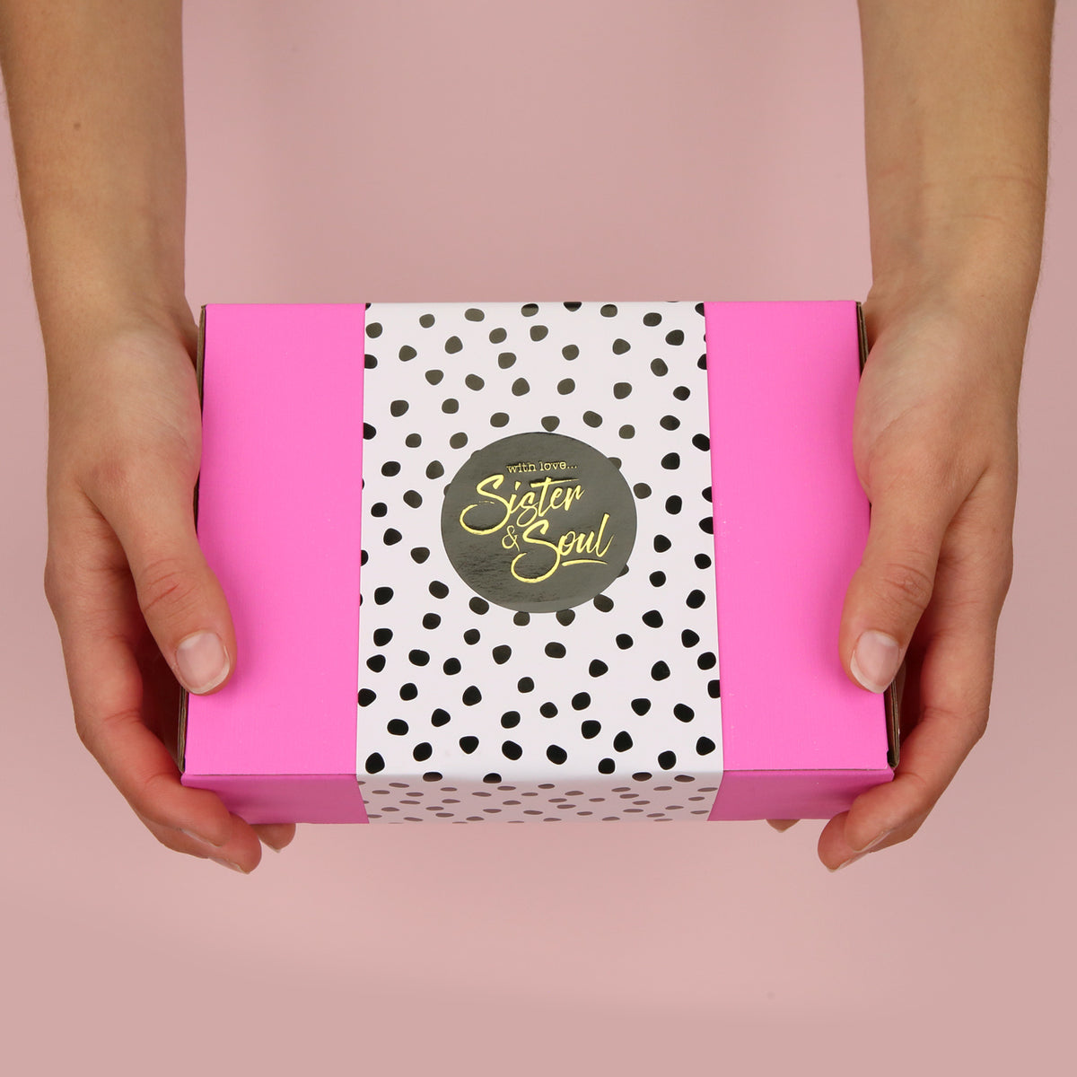 Pink box with black and white potted wrapping and black Sister & Soul sticker, with hands holding it out front on a pink background. 