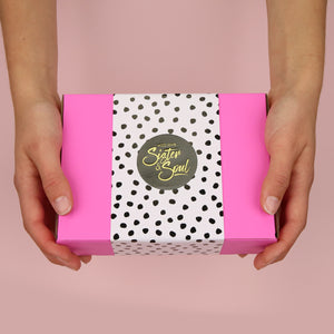 Pink box with black and white potted wrapping and black Sister & Soul sticker, with hands holding it out front on a pink background. 